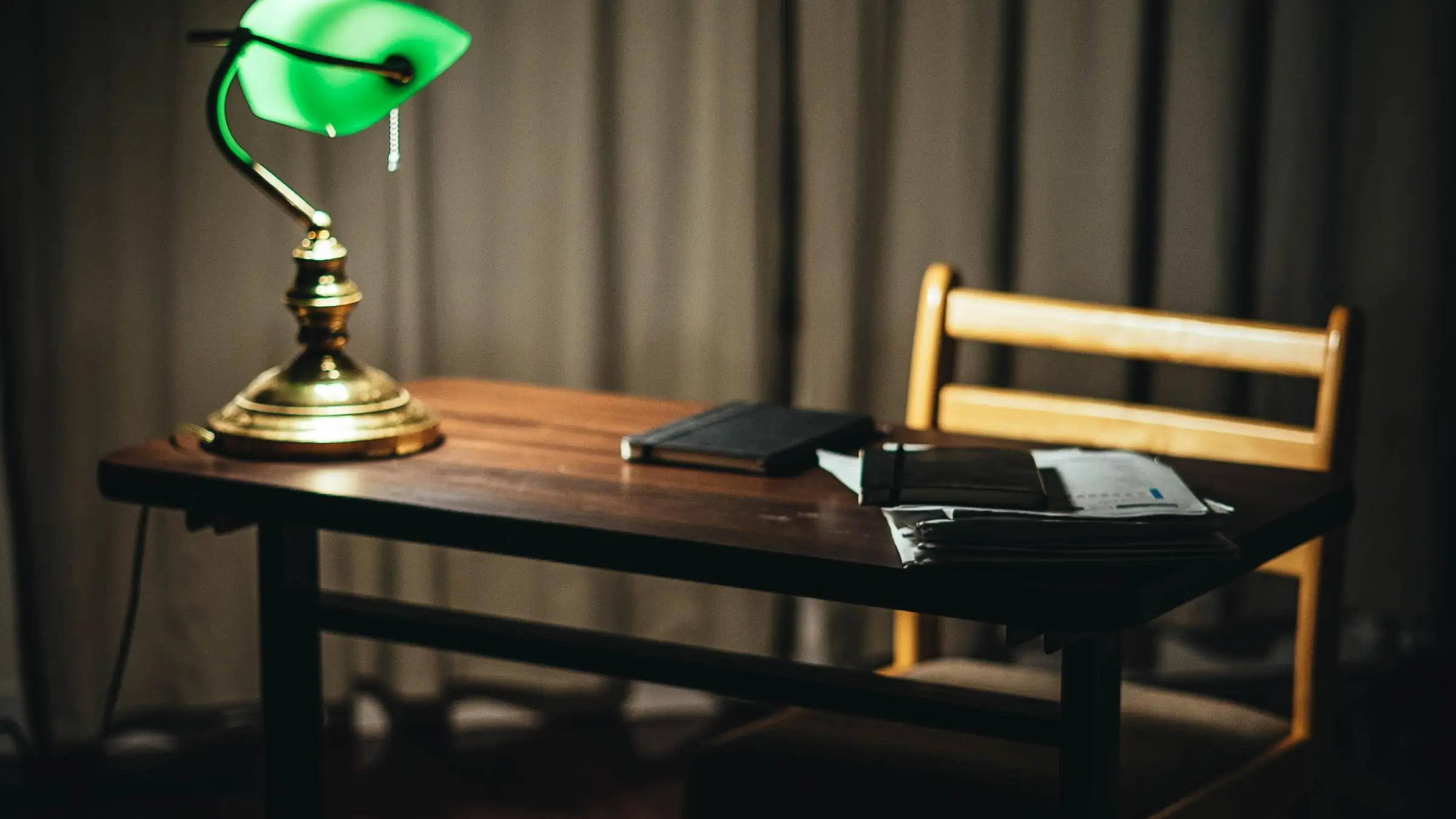 Mesa de despacho de madera con un flexo de biblioteca encendido y unos documentos encima